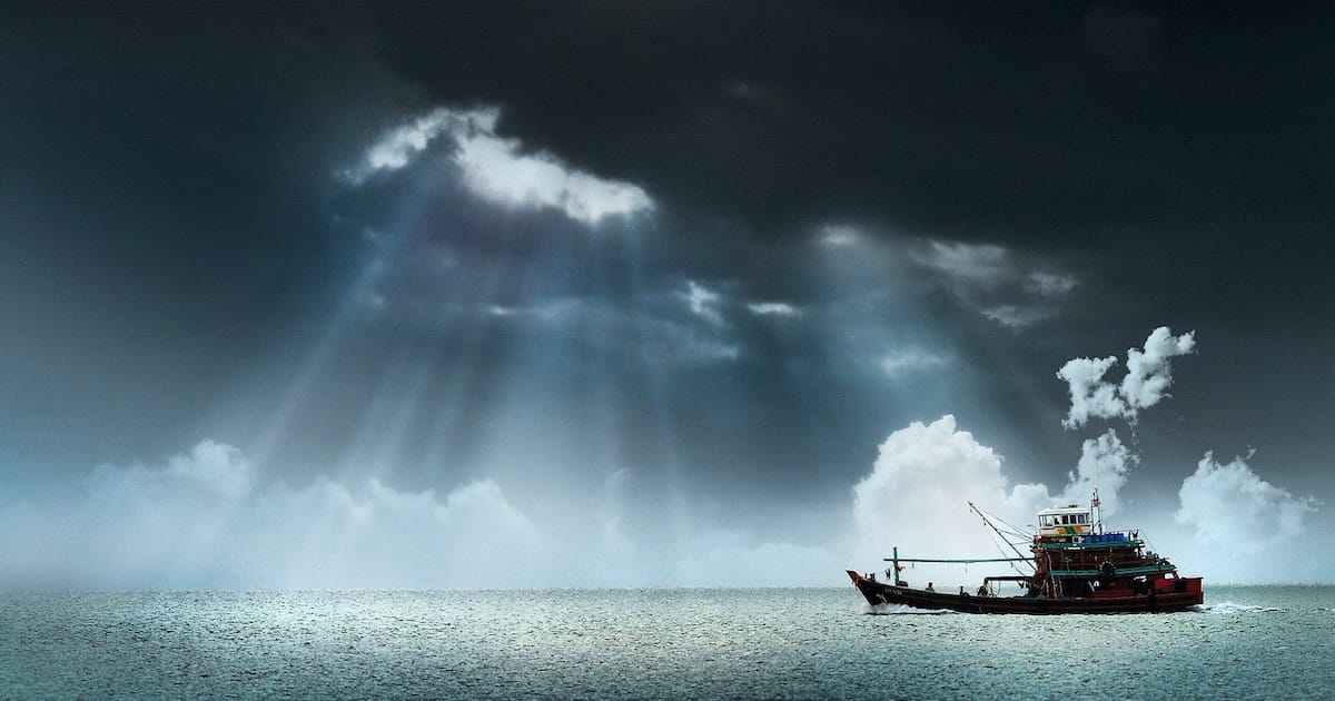 sun rays through the clouds illuminating a boat on the calm sea
