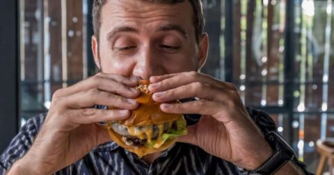 image of man eating juicy burger -- plant-based backlash