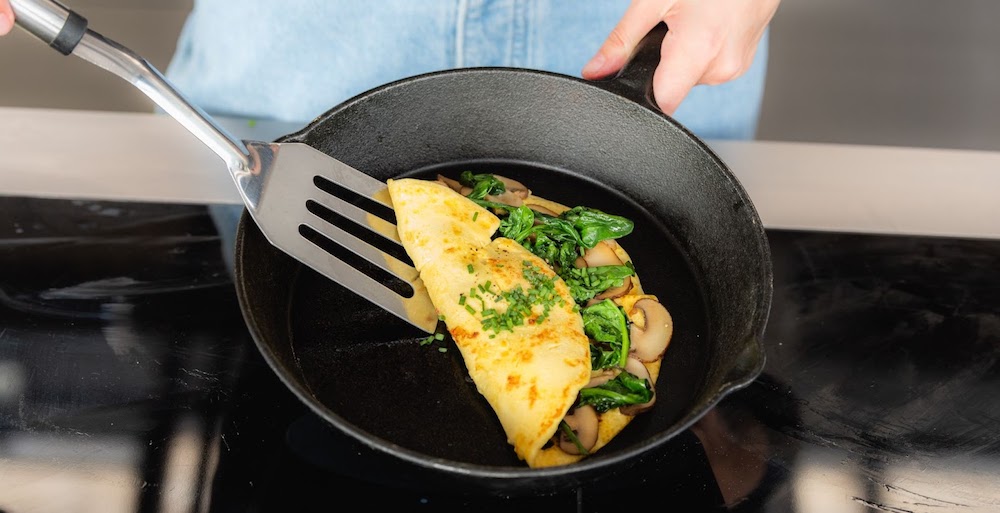 image of omelet in cast iron pan, with mushrooms, folded in half with metal spatula; eggs made with precision fermentation