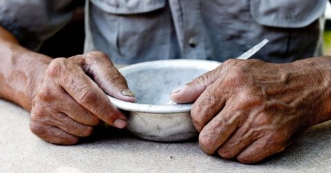 a pair of older-appearing hands grasps a bowl, seated at a table, Blue Zones docuseries debuts on Netflx