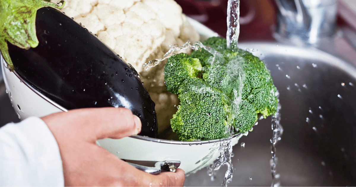 Broccoli, cauliflower and eggplant in a colander being rinsed