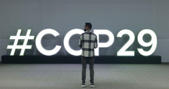 A man stands in front of an illuminated hashtag COP29 logo on day two at the UNFCCC COP29 Climate Conference