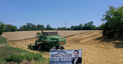 A for sale sign in front of a tractor working on farmland