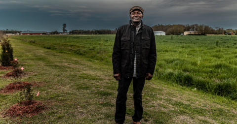 A man standing on his land with factory farms in the background