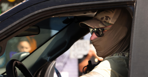 A masked ICE agent driving a car