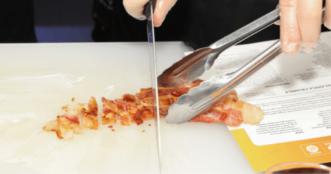 A piece of bacon being chopped with a knife