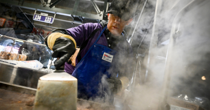 A cook working on a grill that is steaming