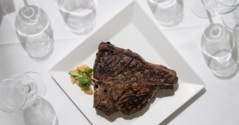 A porterhouse steak on a white plate and white table
