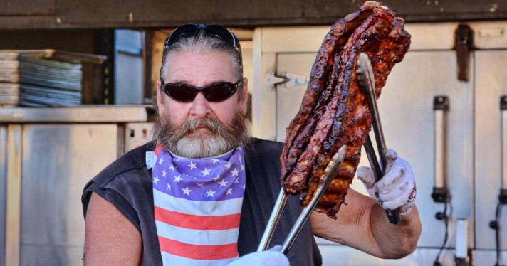 A man holding large chunks of meat with his tongs
