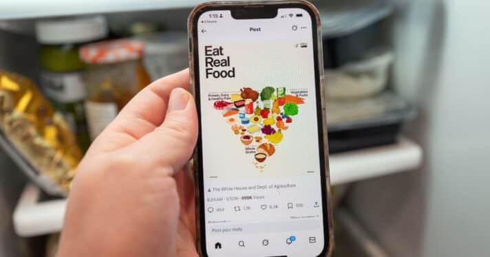 Illustrative image, close-up of a person's hand holding an iPhone displaying a social media post from the US Department of Health and Human Services showing the revised Food Pyramid with caption Eat Real Food