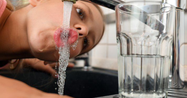 A girl drinking water from a faucet