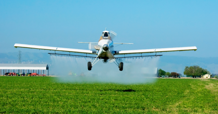 A plane dropping pesticides on a field