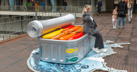 A woman sitting on a large art display of a tin of sardines