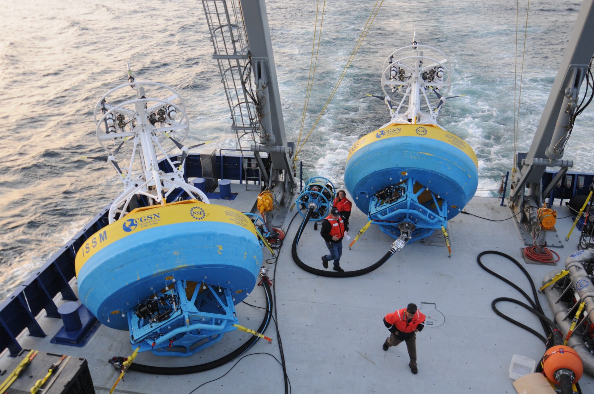 People walking on the deck of a boat with two oceanography machines