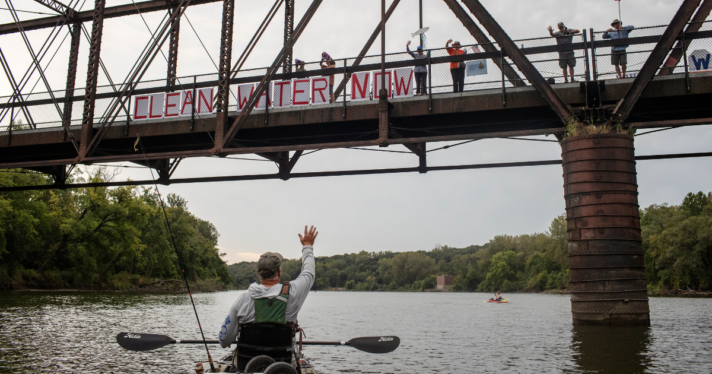 Chris Jones waves to supporters demonstrating for clean water in Des Moines, Iowa. Jones, a retired scientist and water advocate, is running for Iowa’s secretary of agriculture.