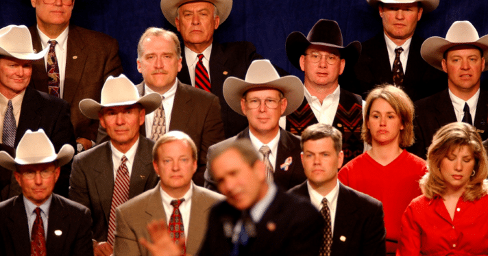 A group of men in cowboy hats along with some women sitting behind George W. Bush giving a speech