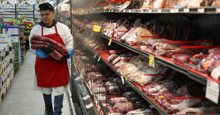 A man carrying a piece of meat into the meat section of a grocery store
