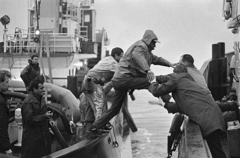 People climbing off a ship onto a smaller boat